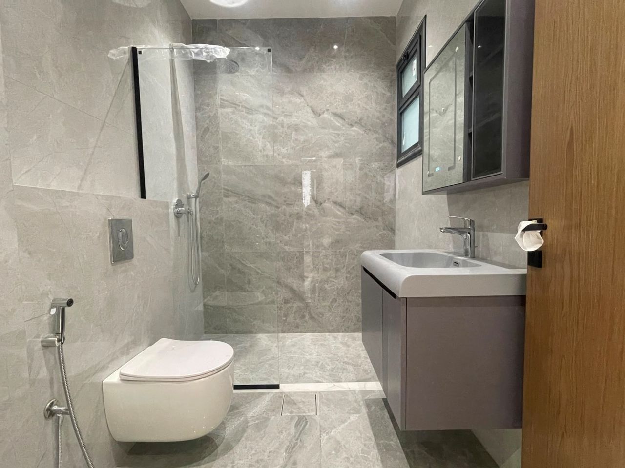 A finished bathroom in large-format stone tile, with a walk-in shower and a wall-hung basin.